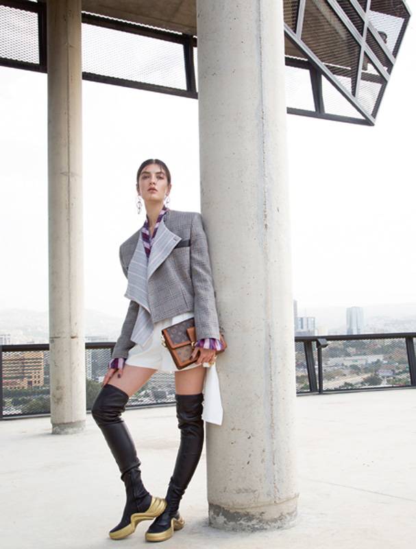 بلوزة ملتفة مع سترة صوفية قصيرة، وشورت مزين على الجانبين، وجزمة عالية، وحقيبة Dauphine.