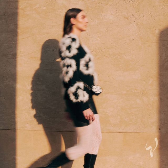 كنزة من الكشمير الأسود والأبيض مزيّنة بالريش. شورت من الجلد الأسود مزيّن بزرّ جوهرة. حقيبة بالأسود والأبيض من البليكسي غلاس والمعدن. جزمة سوداء من القماش والجلد اللمّاع. من شانيل CHANEL Fall-Winter 2023/24 Ready-to-Wear collection