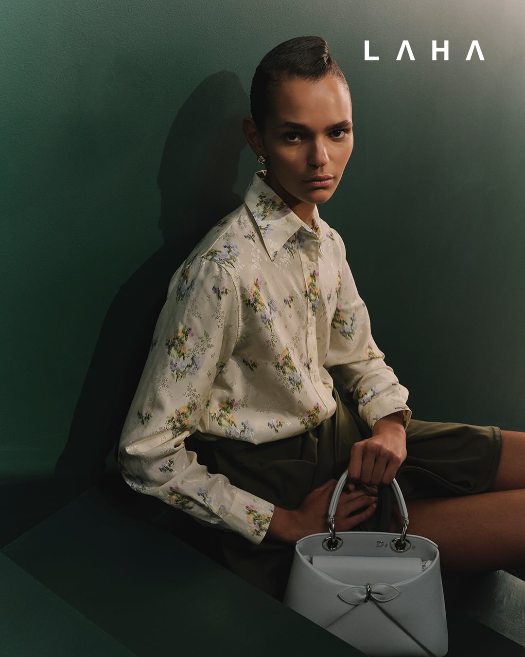 أقراط، قميص بنقشة وردية، تنورة باللون الأخضر الزيتوني وحقيبة Dior Cigale باللون الأزرق من Dior 