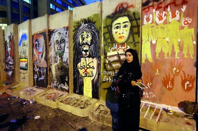 متظاهرة لبنانية وراء جدار العزل الذي نُصب (خلال أيام قليلة فقط) لدواعٍ أمنية بالقرب من السراي الحكومي اللبناني بعد انطلاق التحرّكات الشعبية ضدّ فساد يحرم المواطن أبسط حقوقه.