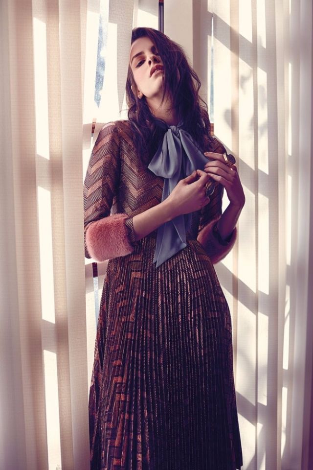 فستان برونزي مطبع مع فرو وردي على طرفي الكمين من Gucci. خاتمان من Pebble London.
