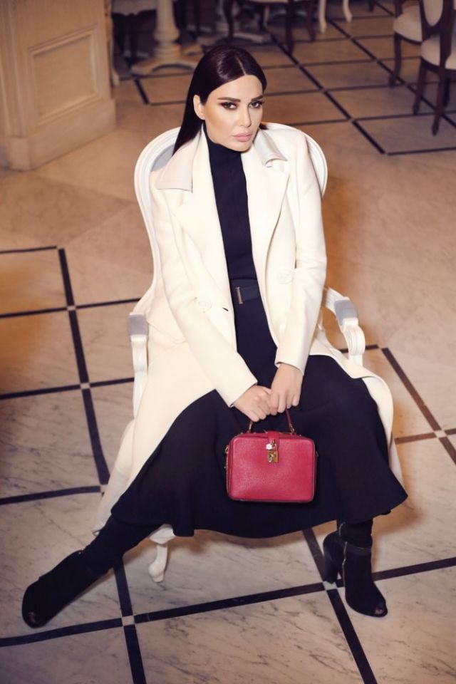 فستان أسود من Victoria Beckham. معطف أبيض من Fendi. حقيبة من الجلد الأحمر من Dolce&Gabbana. جزمة من Elie Saab.
