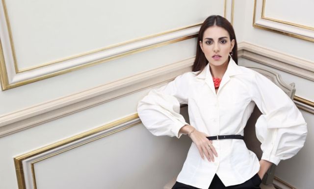 بلوزة مع حزام بكمين منتفخين من الحرير من Carolina Herrera. قلادة من المرجان من Oscar de la Renta.
