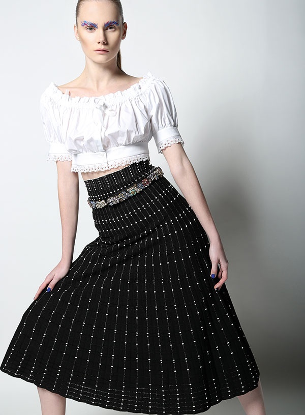 تنورة من النسيج المحبوك وبلوزة بيضاء وحزام مرصع بالحجارة من Alexander McQueen.
