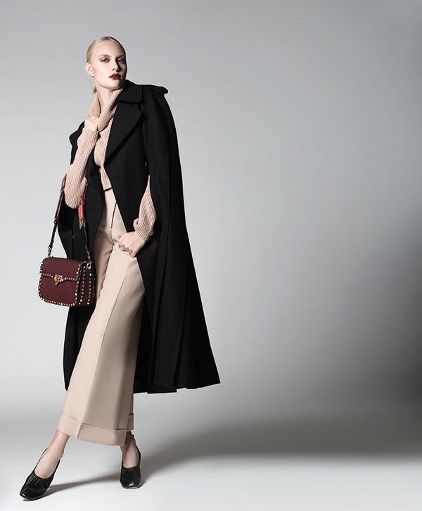 سروال من الكريب البيج، وكنزة باللون البيج، ورداء أسود وحقيبة من الجلد المزين بالمسامير. الكل من Valentino. حذاء من Celine.
